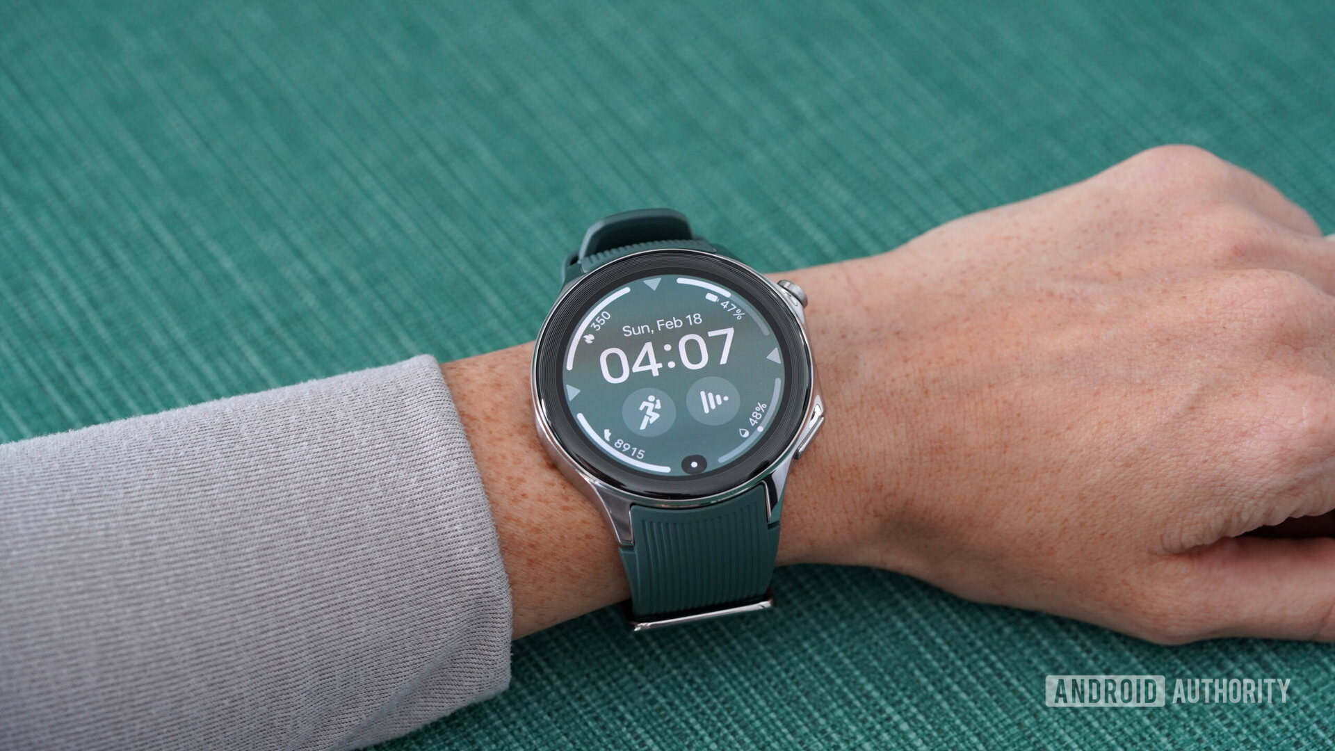 A OnePlus Watch 2 displays a watch face, which emphasizes the device's large bezel.